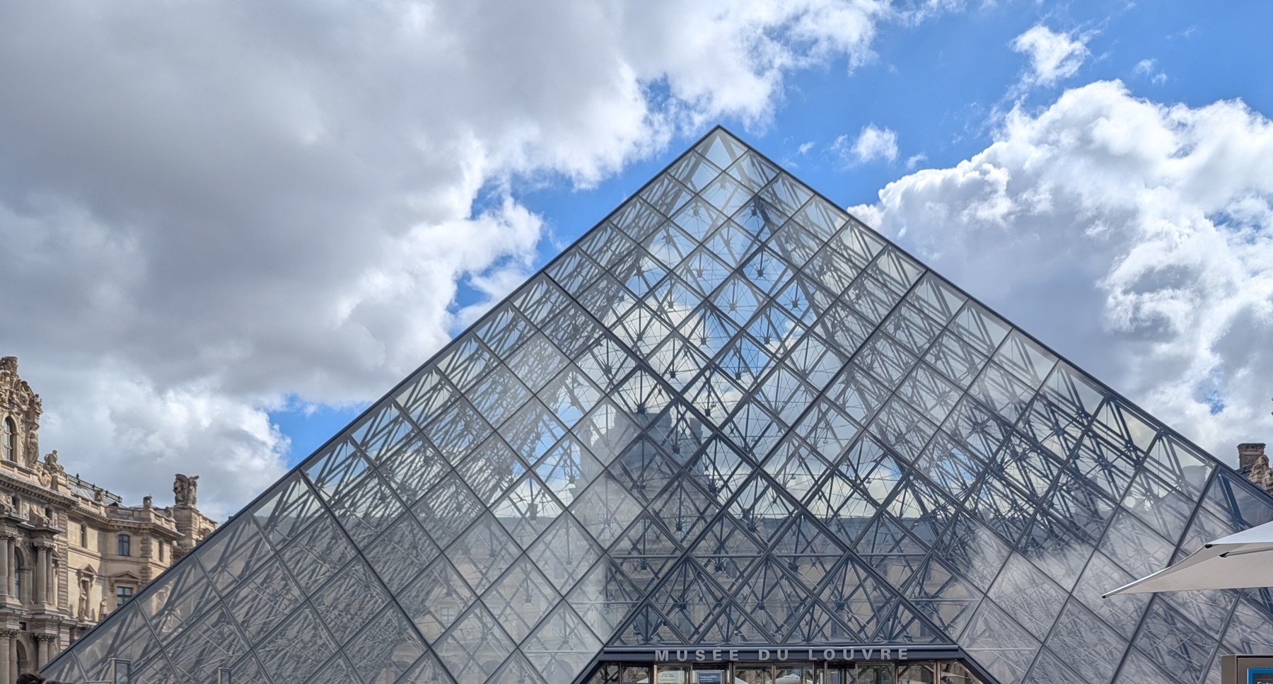 The Louvre glass pyramid beneath a cloud-filled Paris sky